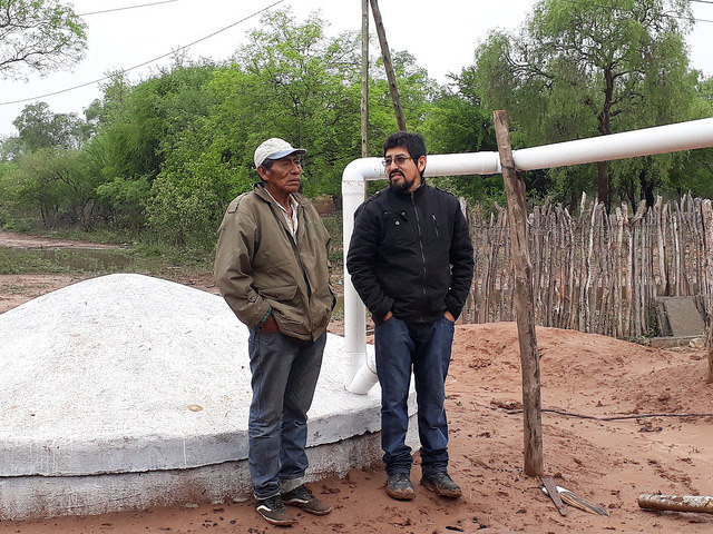 Mariano Barraza of the Wichí indigenous community (L) and Enzo Romero, a technician from the Fundapaz organisation, stand next to the tank built to store rainwater in an indigenous community in the province of Salta, in the Chaco ecoregion of northern Argentina, where there are six months of drought every year. CREDIT: Daniel Gutman/IPS
