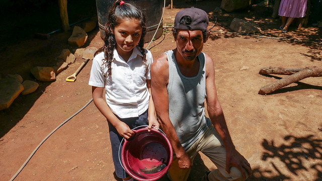 Cristino Martínez and one of his daughters show the tilapia they have just caught in the family pond they have dug in the backyard of their home in the village of El Guarumal in the eastern department of Morazán, El Salvador. The large peasant family raises fish for their own consumption and not for sale. CREDIT: Edgardo Ayala/IPS