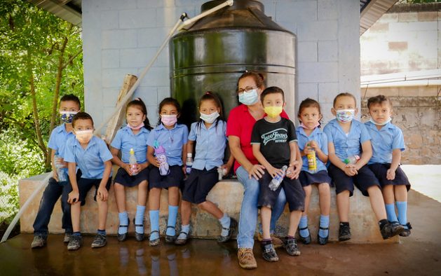 Angélica María Posada, a teacher and school principal in the village of El Guarumal, in eastern El Salvador, poses with primary school students in front of the school where they use purified water collected from rainfall, as part of a project promoted by FAO and Mexican cooperation funds. The initiative is being implemented in the countries of the Central American Dry Corridor. CREDIT: Edgardo Ayala/IPS