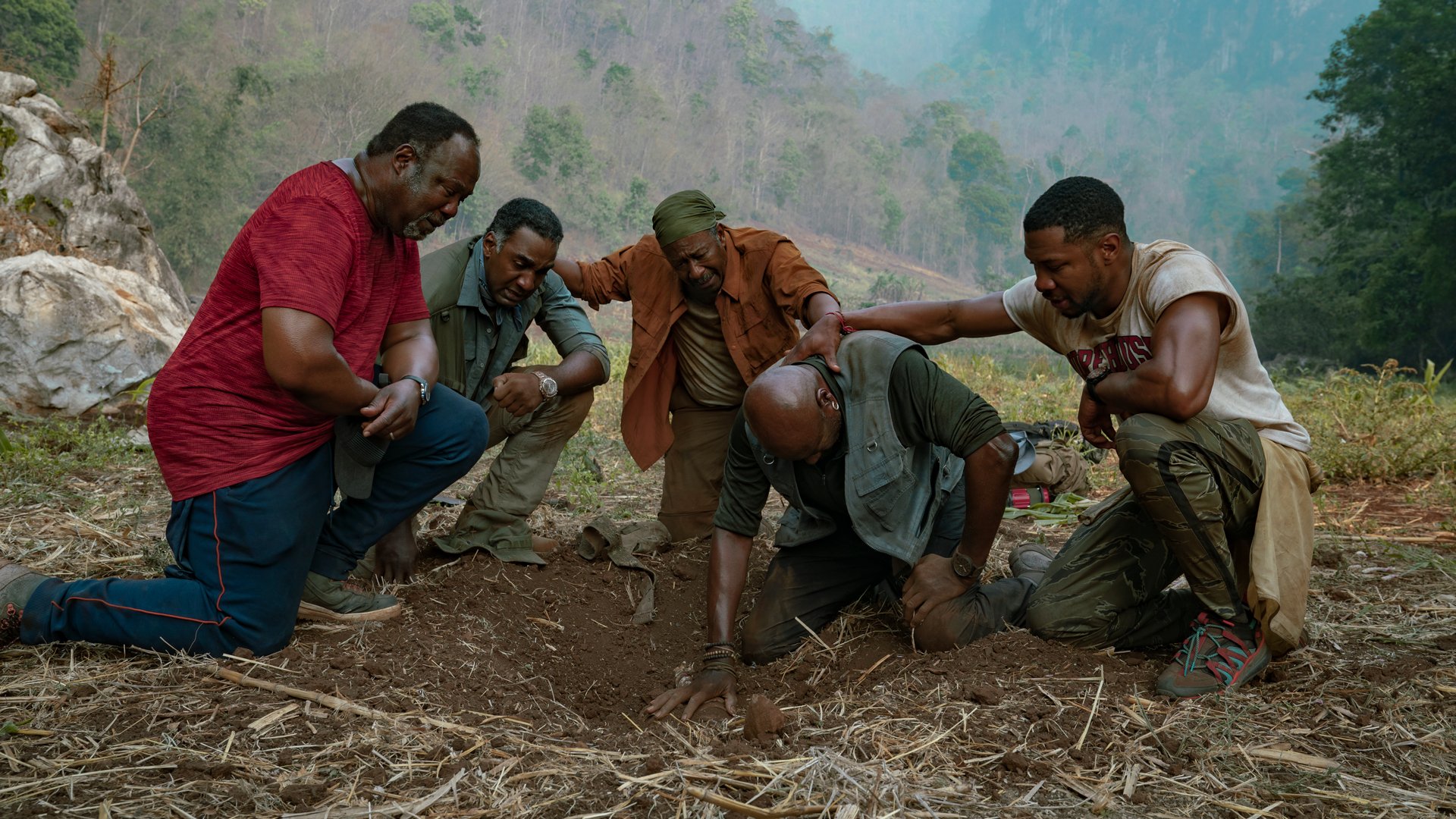 Five men look into a shallow newly dug hole in the middle of the wilderness.