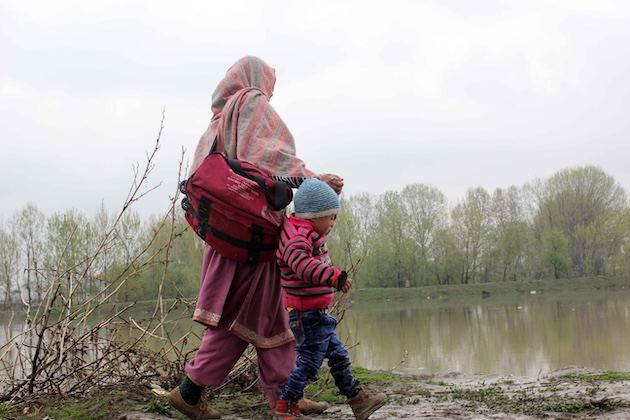A woman in a remote hamlet in Kashmir, India, migrates to a safer location with her child as floodwater inundates her hometown. Credit: Umar Manzoor Shah/IPS